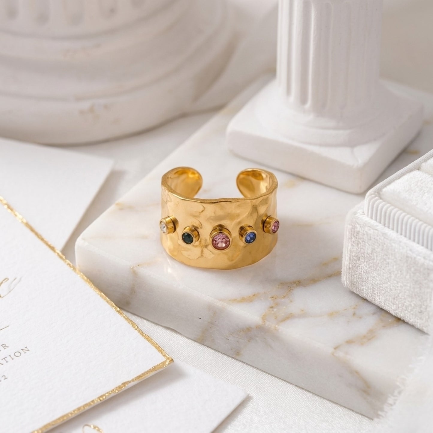 BEHI AZZU 18k PVD gold plated stainless steel adjustable size ring with multiple colored Zircon gemstones set around its circumference.