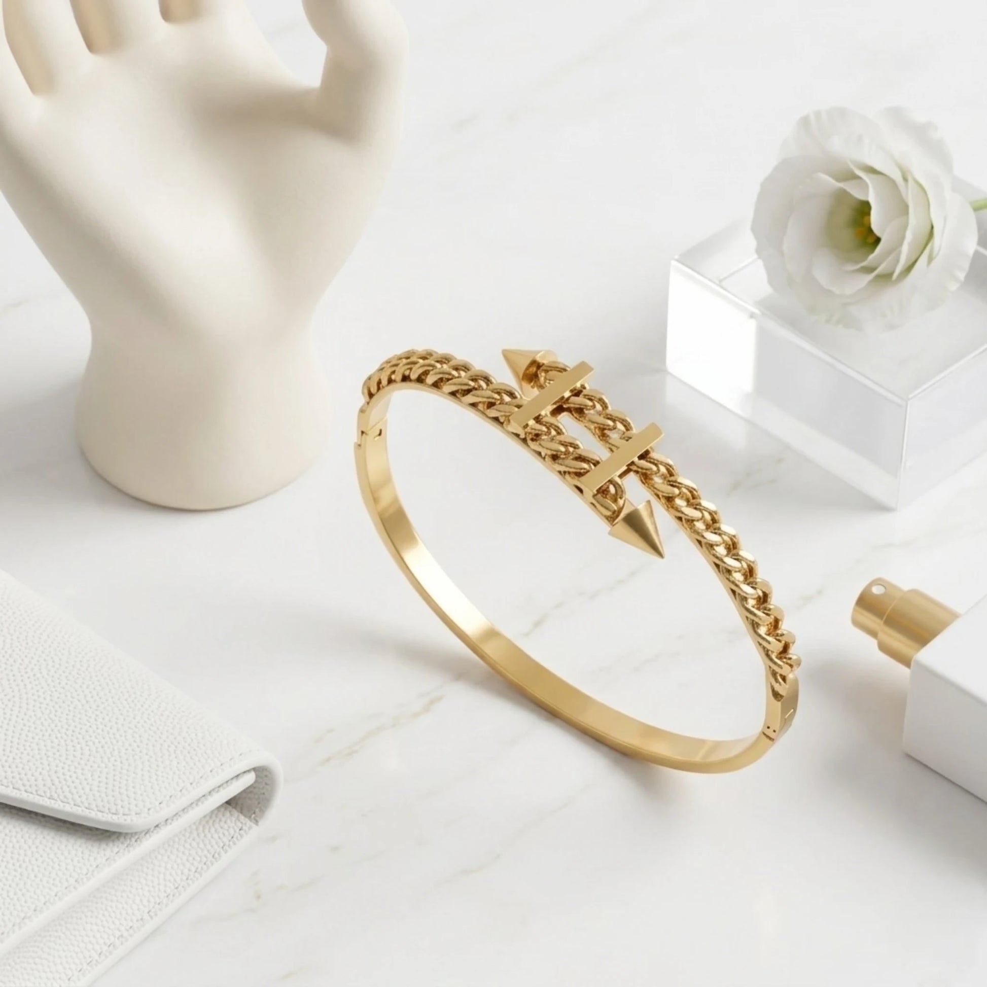 BEHI MILANO Alane Bracelet gold flat lay on marble — curb chain spike bangle with hand display prop and white flower, 18k gold-plated jewelry