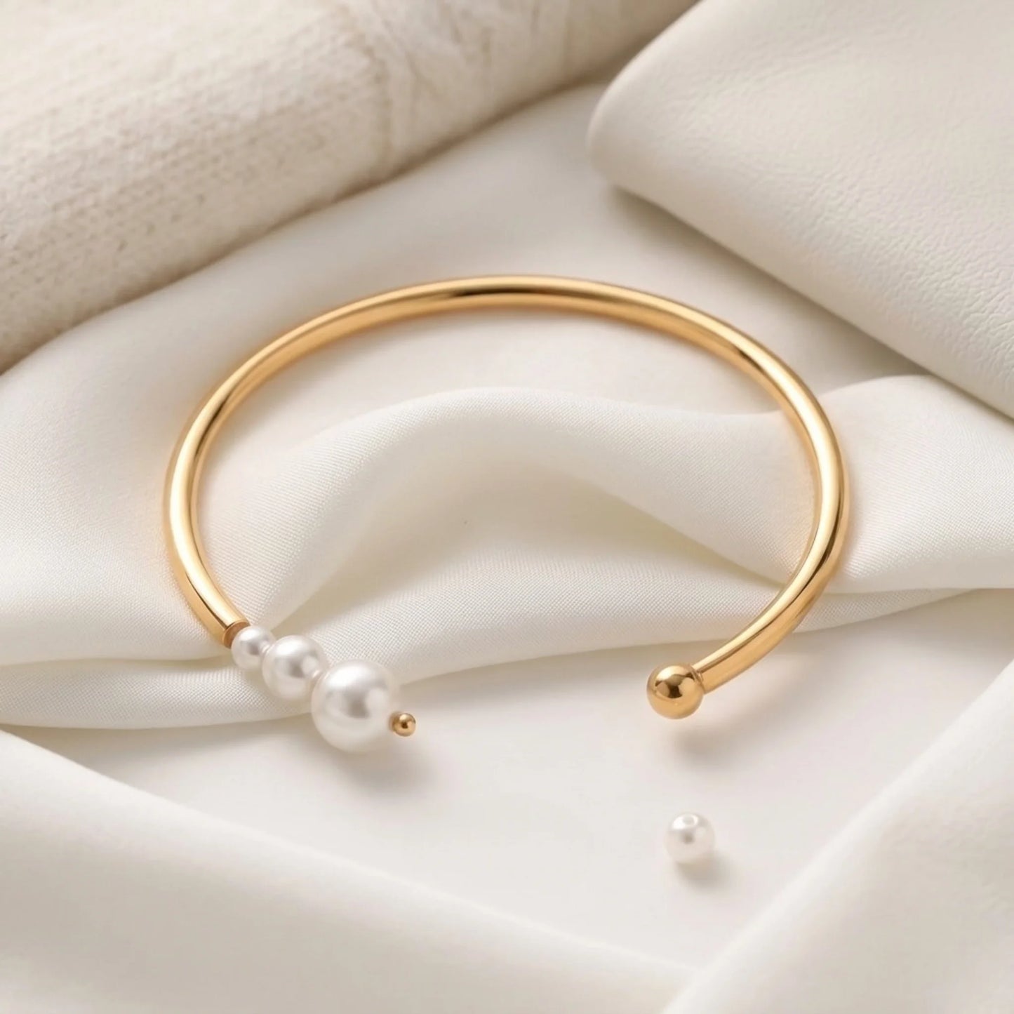 BEHI MILANO Alba Bracelet flat lay on cream silk — 18k gold-plated open cuff bangle with pearl cluster, tarnish-free waterproof fine jewelry