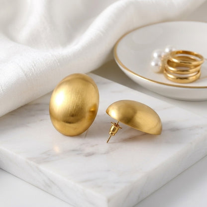 BEHI MILANO Annarita Earrings — detailed glossy finish view of gold oval statement studs on marble