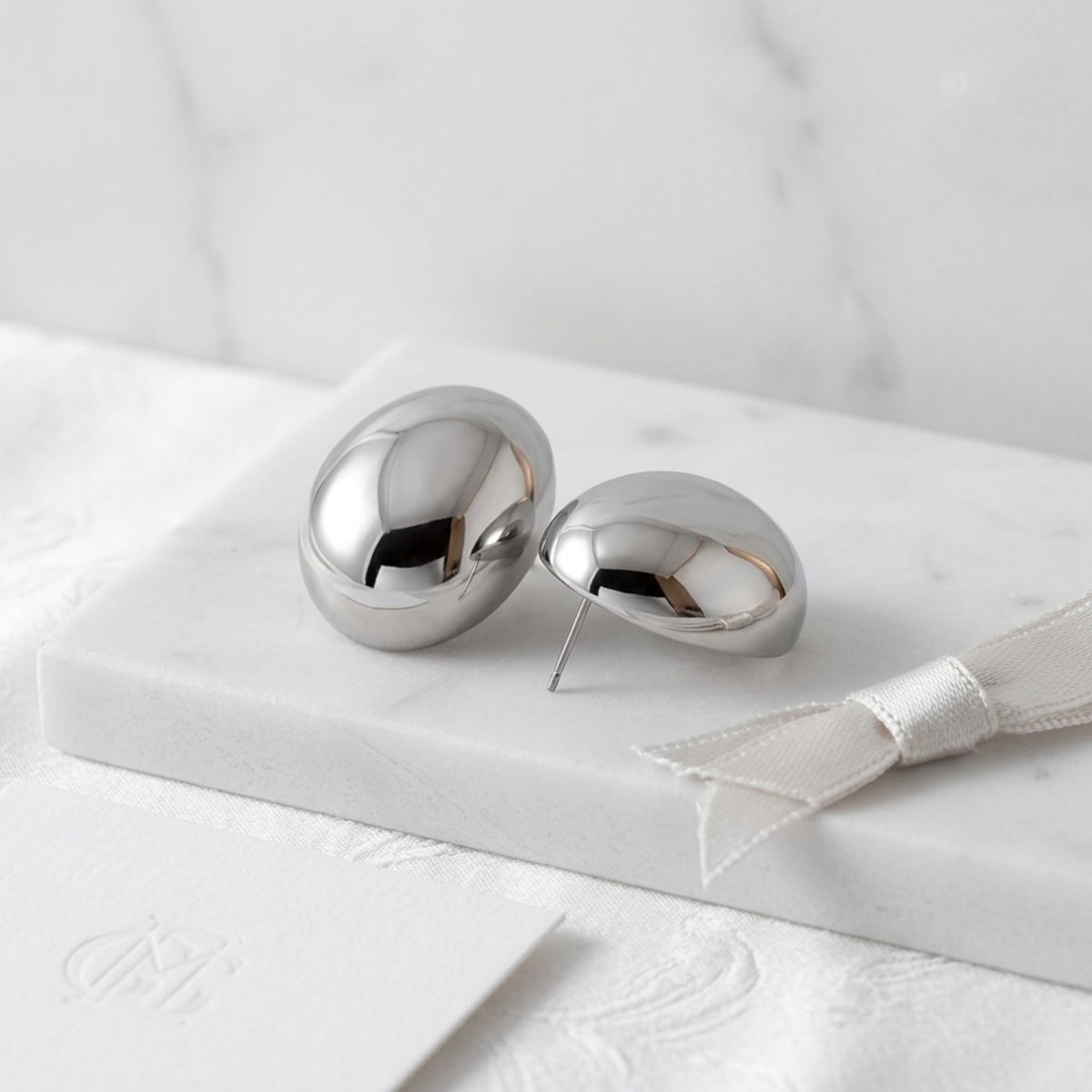 BEHI MILANO Annarita Earrings — silver stainless steel oval dome studs on white marble