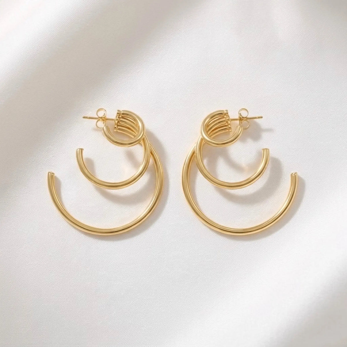 BEHI MILANO Ariel Earrings — pair of 18k gold multi-ring hoop earrings on white silk