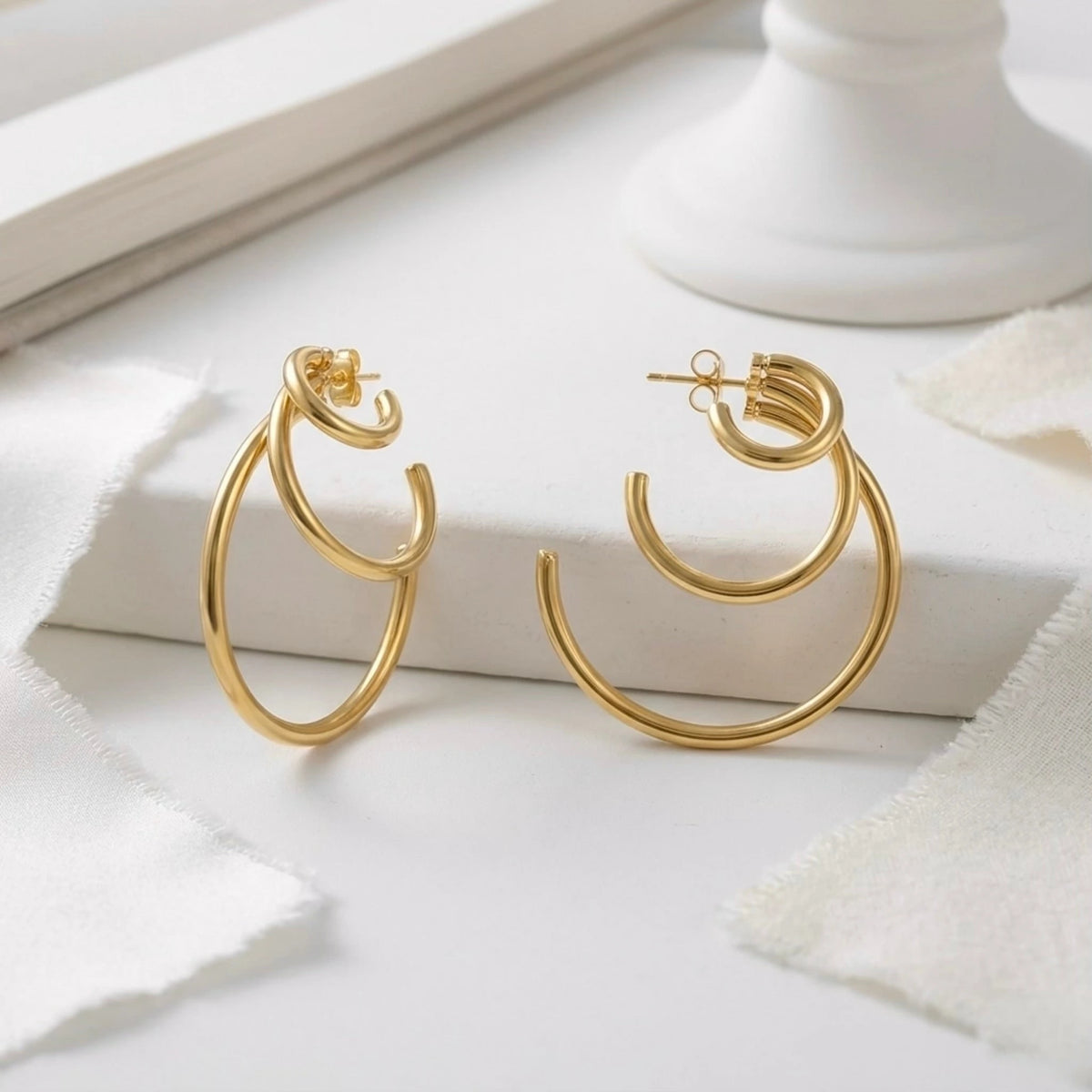 BEHI MILANO Ariel Earrings — 18k gold triple hoops displayed on white marble with sheer ribbon