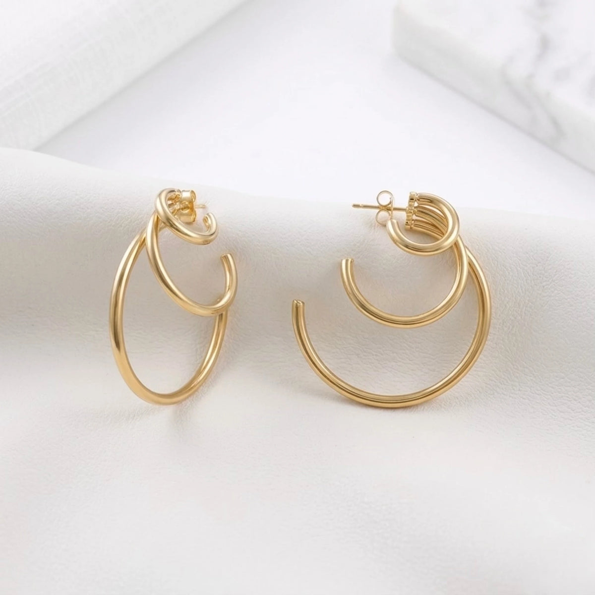 BEHI MILANO Ariel Earrings — 18k gold multi-tier hoops on white draped silk fabric