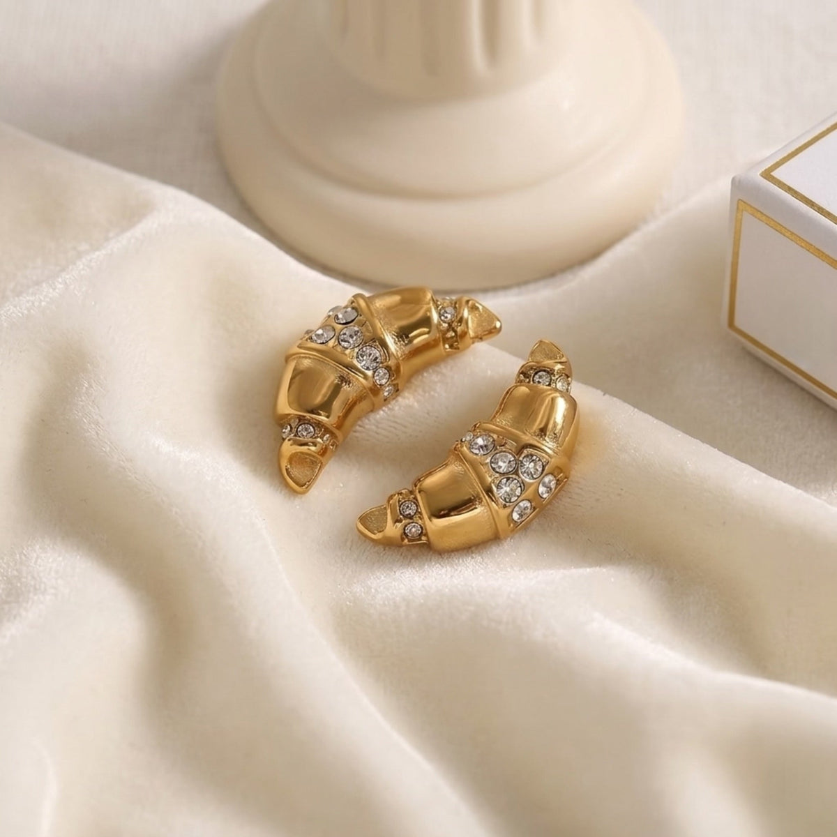 BEHI MILANO Aris Earrings — pair of 18k gold zircon croissant earrings on soft white silk fabric