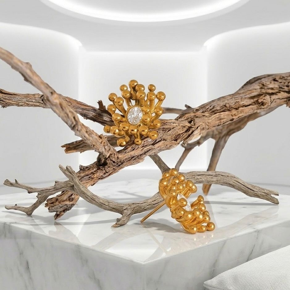 BEHI MILANO Artymanos Earrings — single gold crystal sunburst stud styled on natural branch and marble