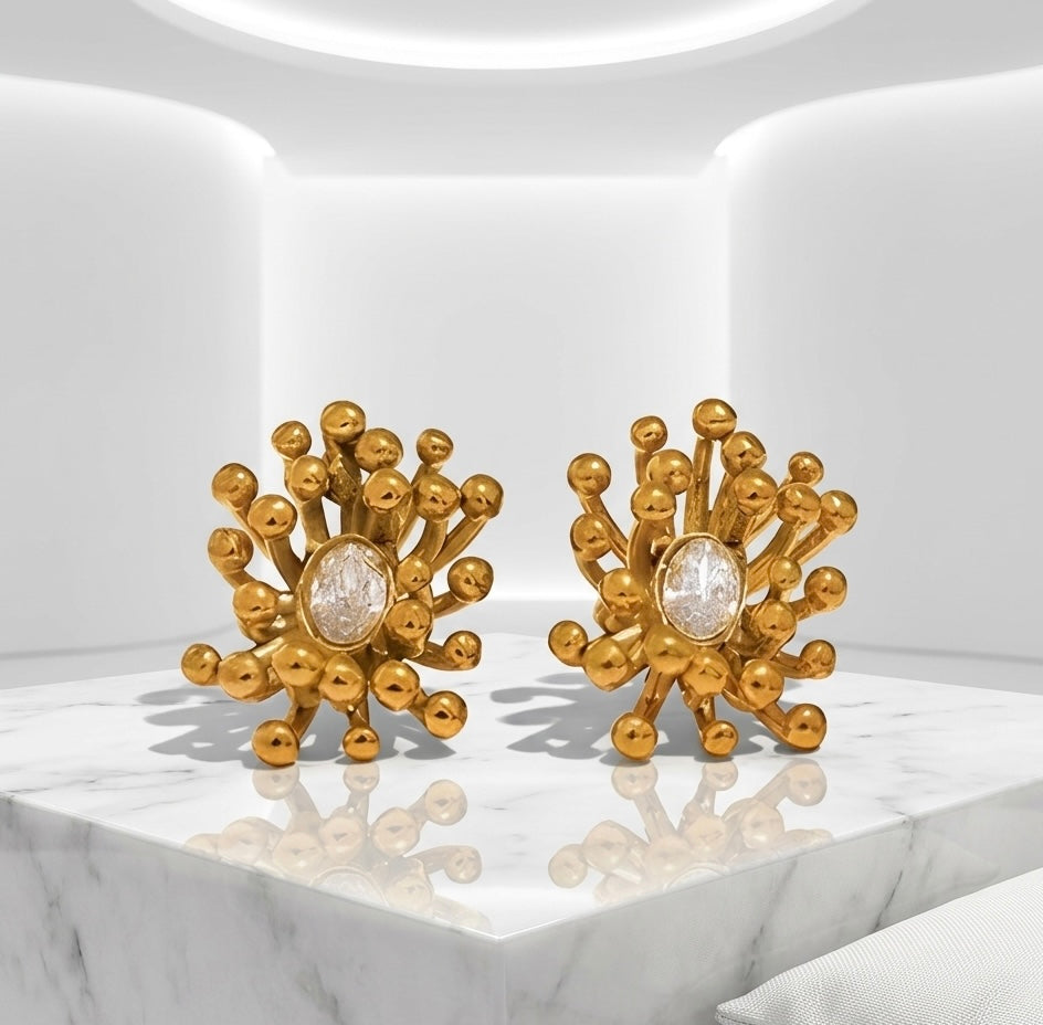 BEHI MILANO Artymanos Earrings — pair of gold sunburst earrings on architectural marble studio pedestal