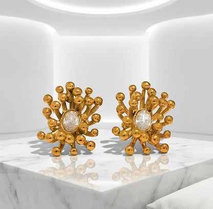 BEHI MILANO Artymanos Earrings — pair of gold sunburst earrings on architectural marble studio pedestal