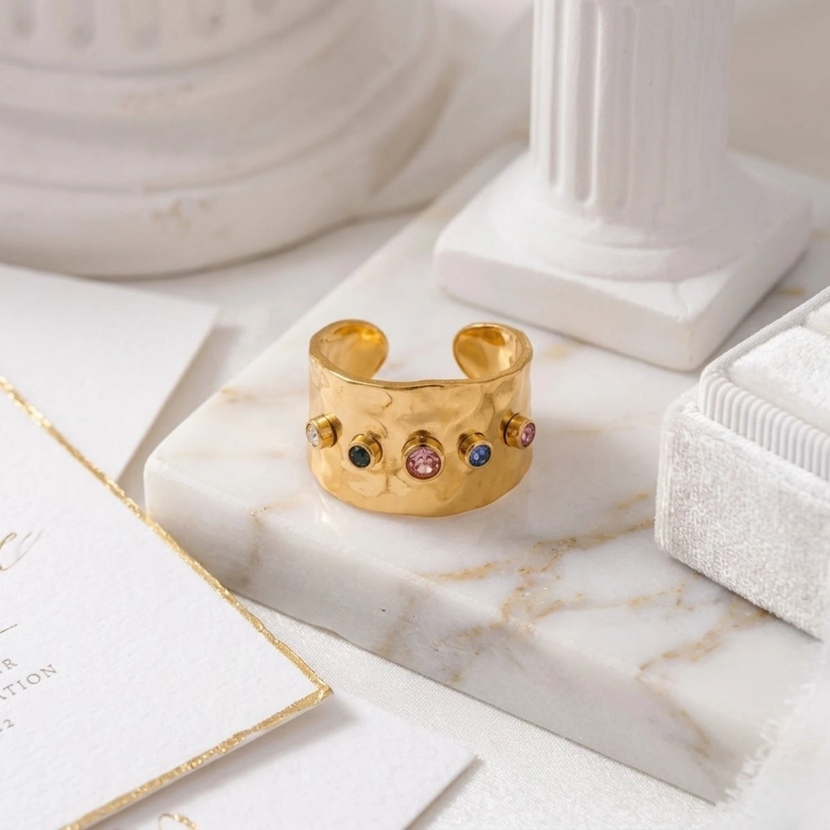BEHI MILANO Azzu Ring — wide gold multi-color stone ring displayed on white marble with architectural column