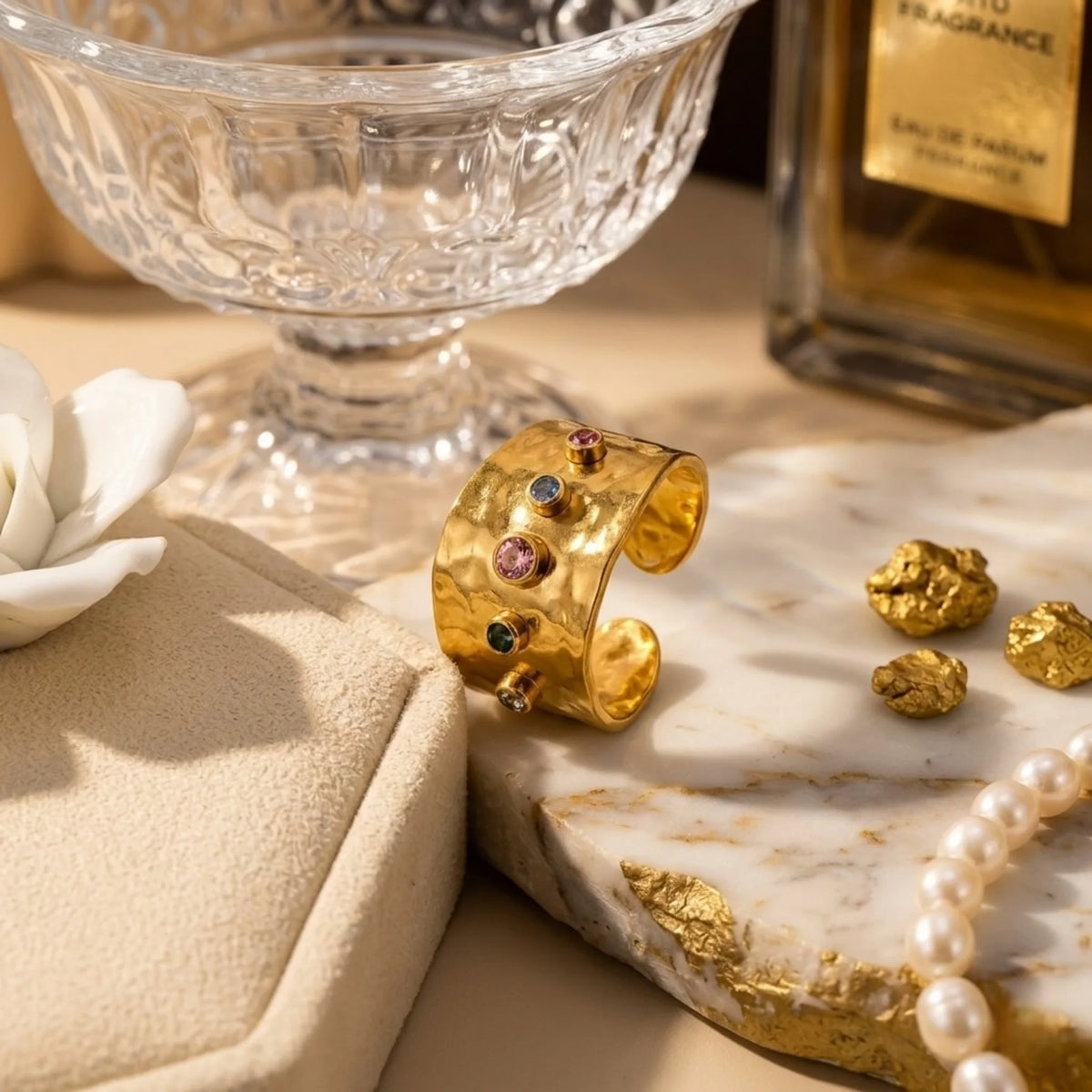 BEHI MILANO Azzu Ring — gold gemstone band on marble tray with pearl strand and luxury perfume bottle
