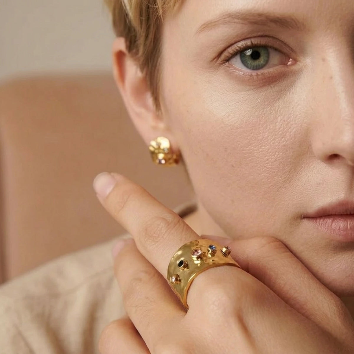 BEHI MILANO Azzu Ring — close-up of model holding hand near face showing gold gemstone band ring