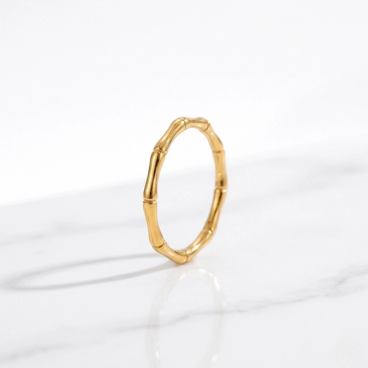 BEHI MILANO Bamboo Ring — thin gold bamboo ring standing vertically on white marble background