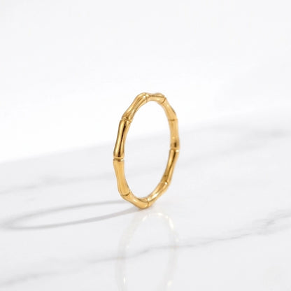 BEHI MILANO Bamboo Ring — thin gold bamboo ring standing vertically on white marble background