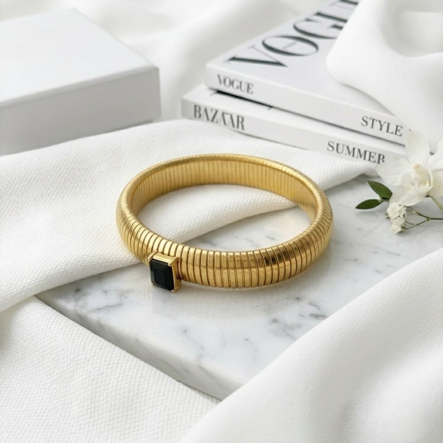 BEHI MILANO Beatriz Bracelet in Black — gold stretch cuff with black onyx gem on marble next to Vogue magazine