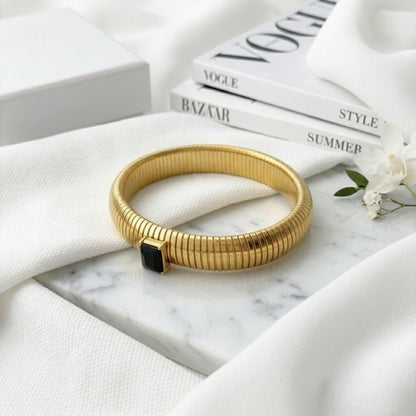 BEHI MILANO Beatriz Bracelet in Black — gold stretch cuff with black onyx gem on marble next to Vogue magazine