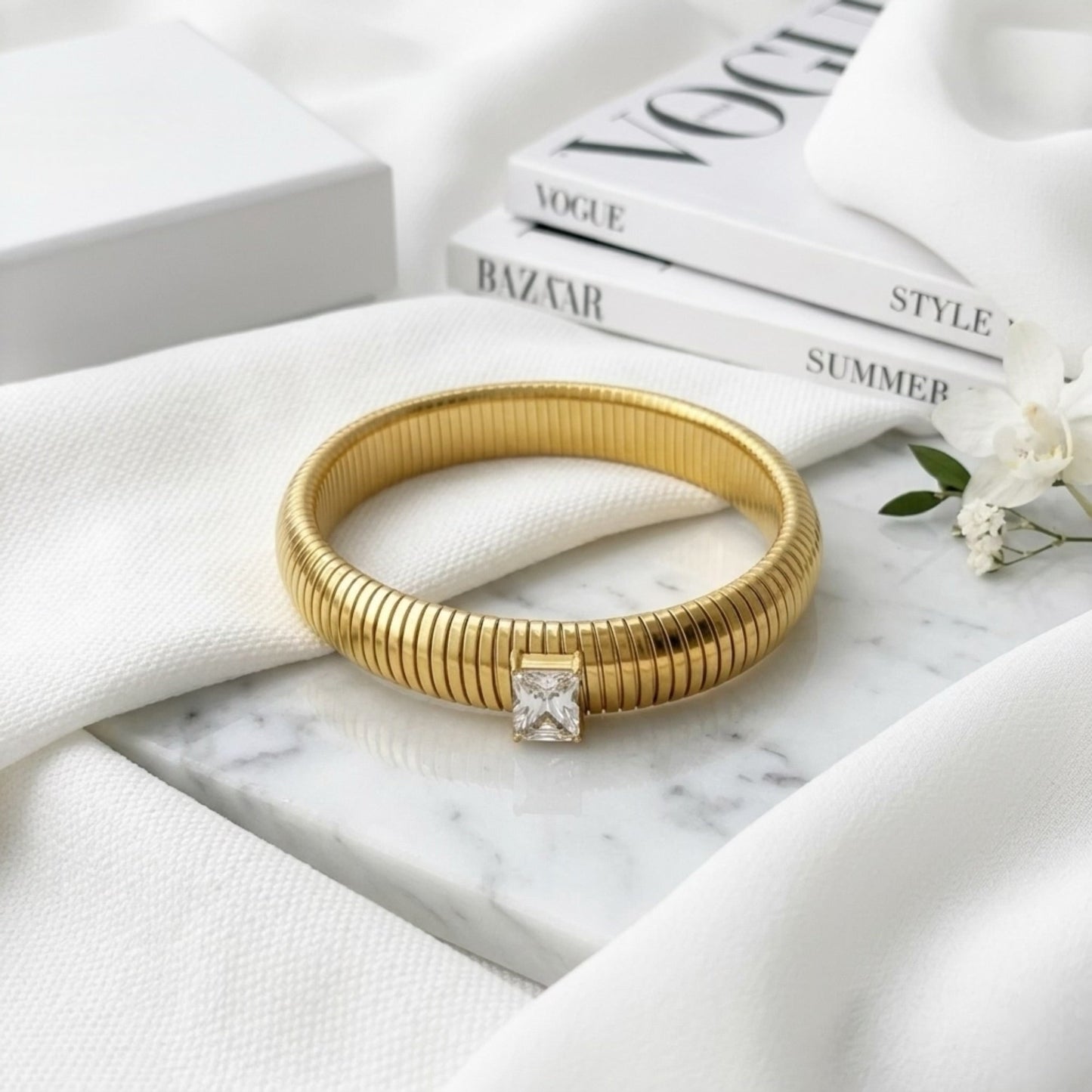 BEHI MILANO Beatriz Bracelet in White — gold stretch cuff with clear gem on marble next to Vogue magazine