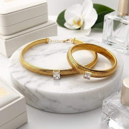 BEHI MILANO Beatriz Jewelry Set — gold ribbed choker necklace and matching stretch bracelet on marble pedestal