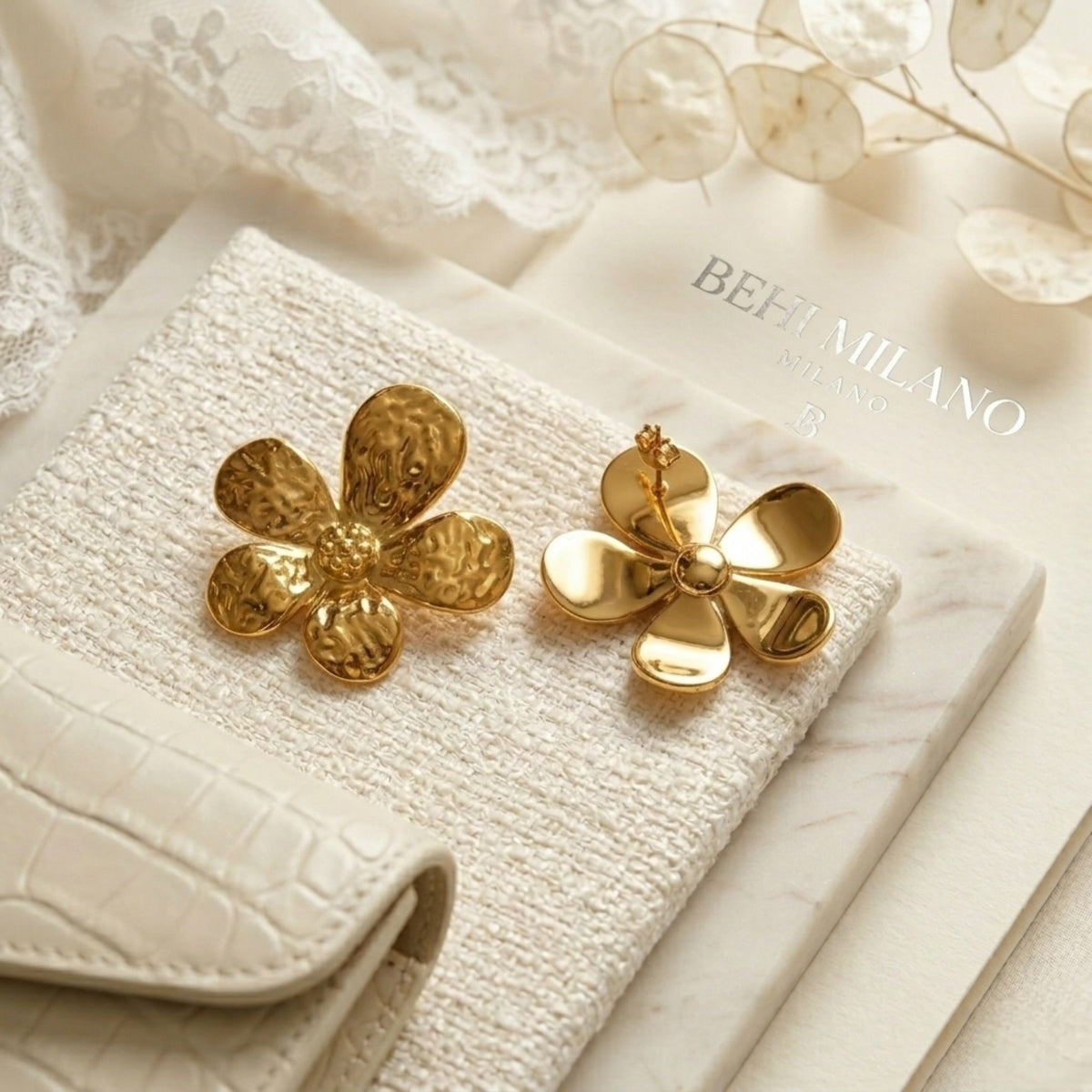 BEHI MILANO Bloom Earrings — pair of 18k gold-plated flower studs on white textured background