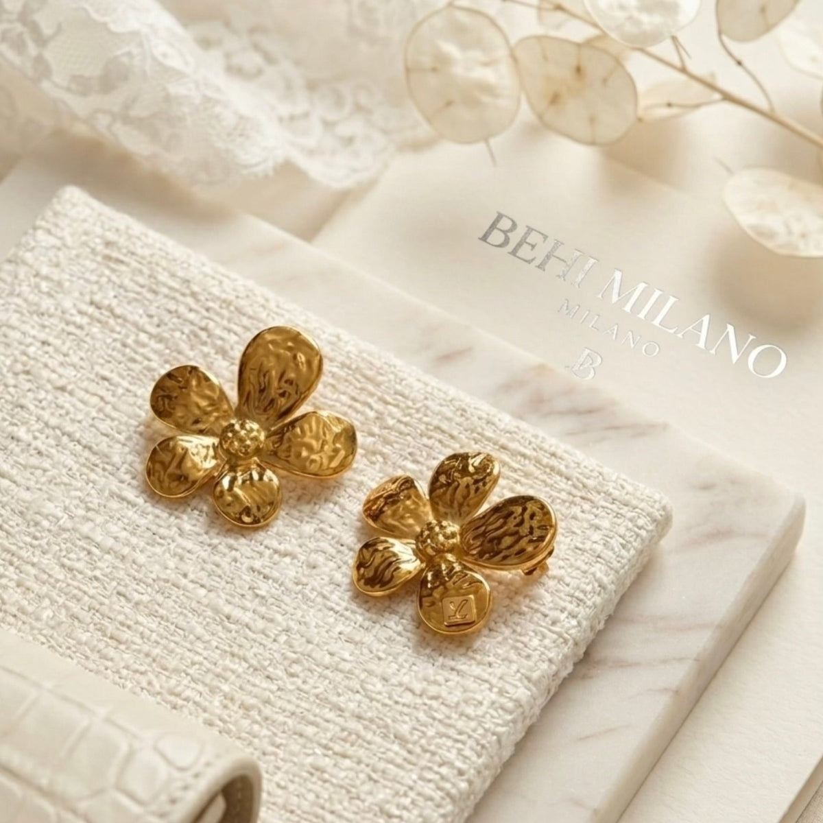 BEHI MILANO Bloom Earrings — detailed close-up of gold hammered petal texture on white leather