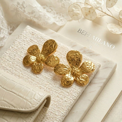 BEHI MILANO Bloom Earrings — gold floral earrings displayed on white croco leather clutch and fabric
