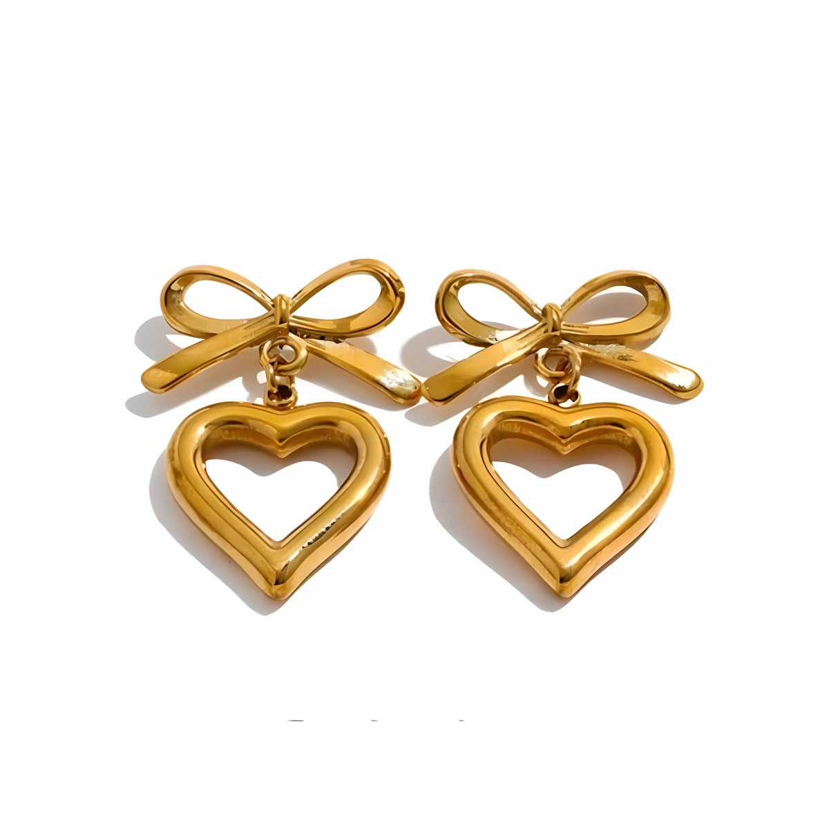 BEHI MILANO Cara Earrings — 18k gold-plated bow studs with open heart drop charms on white background