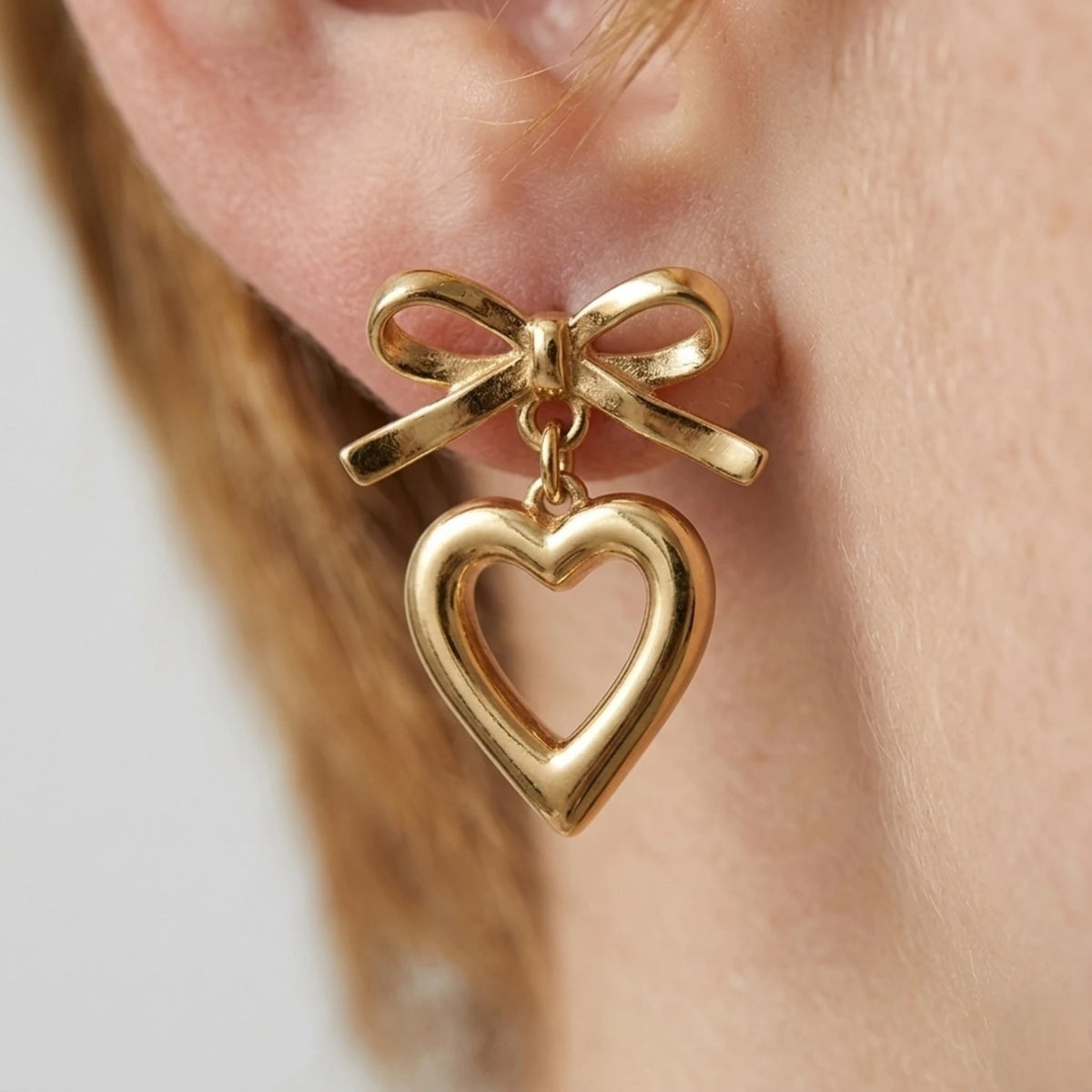 BEHI MILANO Cara Earrings — detailed ear close-up of 18k gold-plated bow and heart drop earring