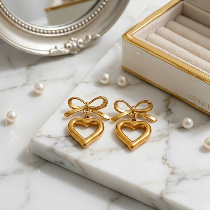 BEHI MILANO Cara Earrings — gold bow heart drop earrings on marble tray with pearls and jewelry box
