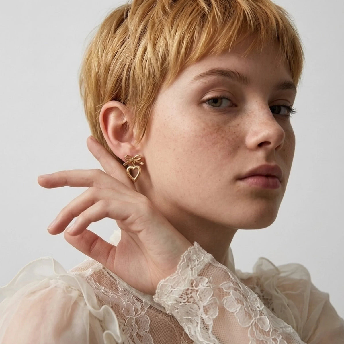 BEHI MILANO Cara Earrings — model wearing gold ribbon and open heart drop earrings