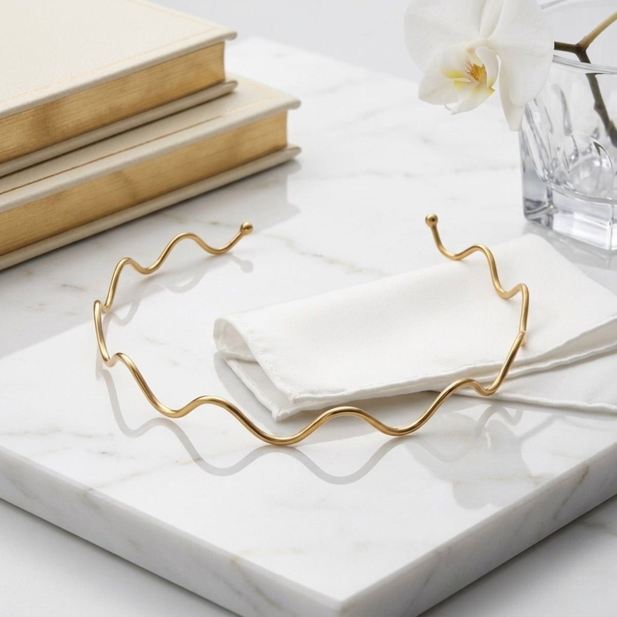BEHI MILANO Carla Choker — 18k gold wave necklace flatlay on marble tray with white cloth