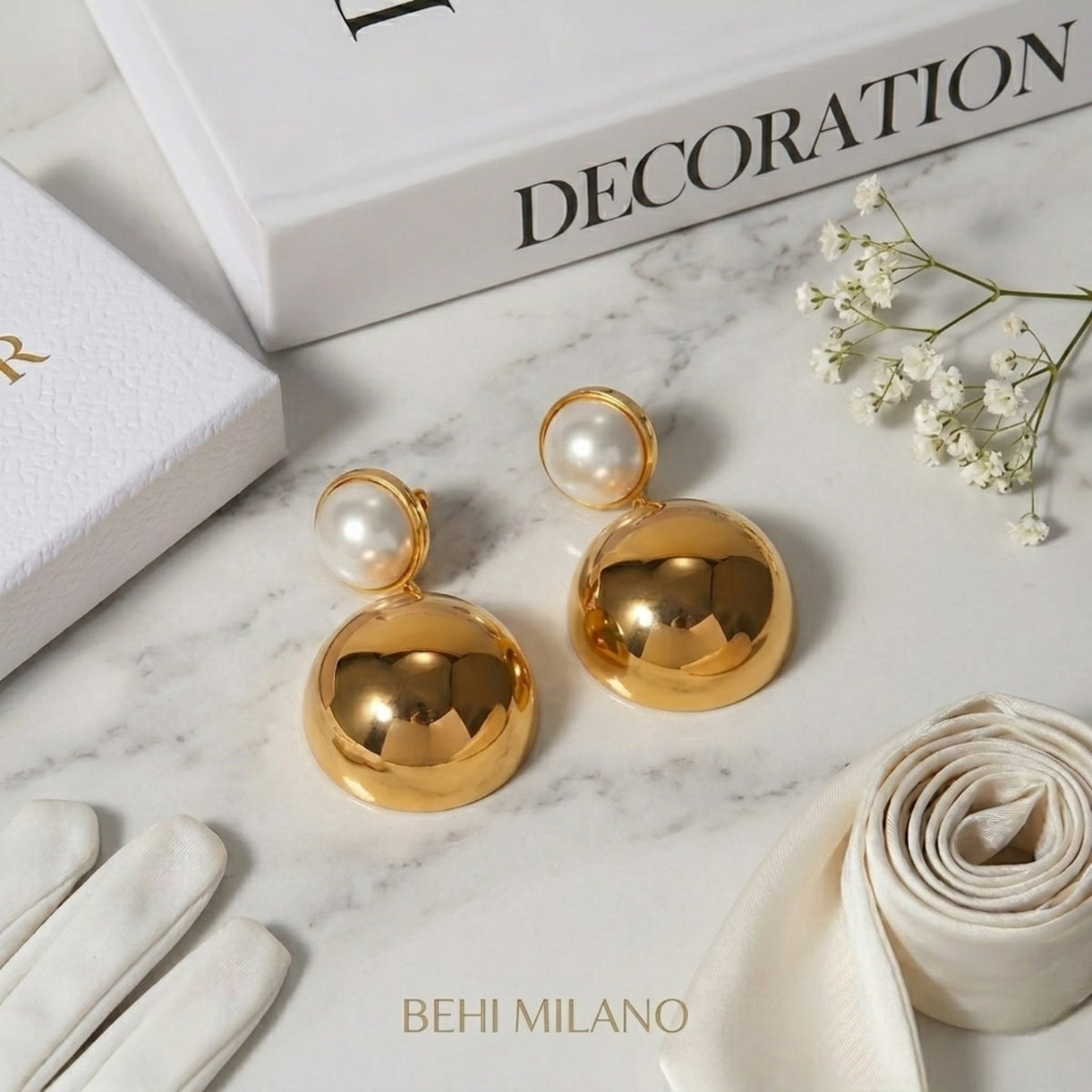 BEHI MILANO Carollina Earrings — gold sphere earrings on white marble tray with silk ribbon and book