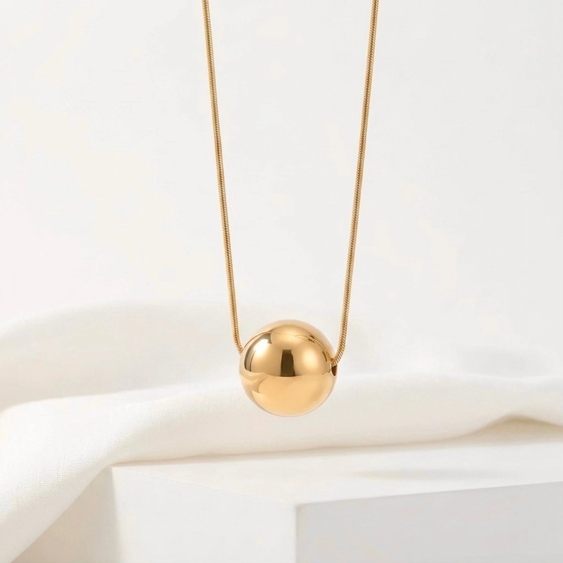 BEHI MILANO Chic Necklace — close-up of mirror-polished gold sphere pendant on white pedestal