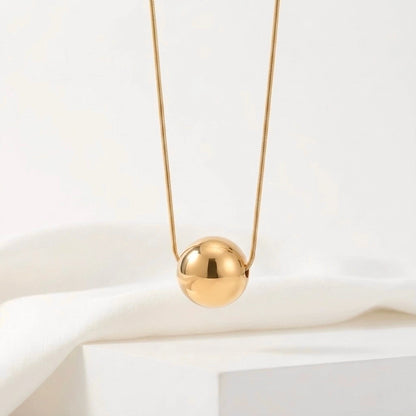 BEHI MILANO Chic Necklace — close-up of mirror-polished gold sphere pendant on white pedestal