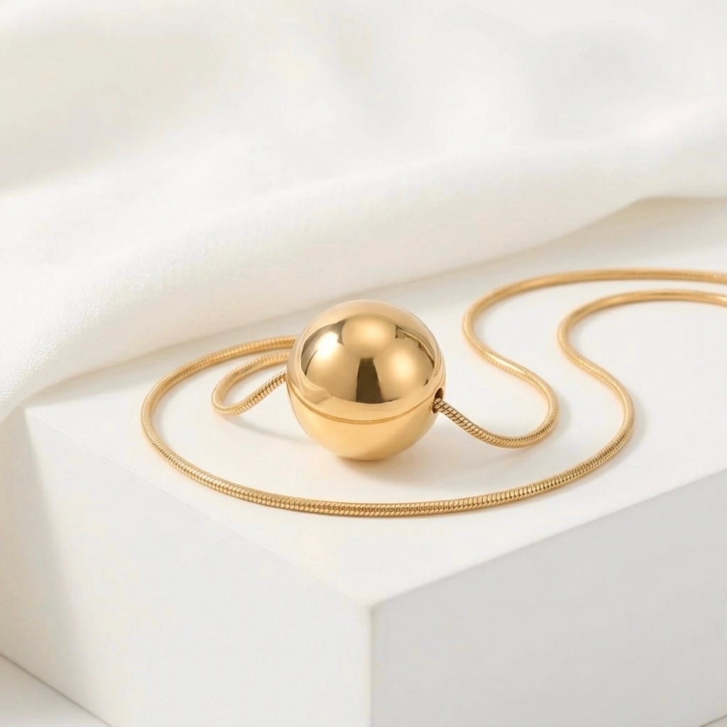 BEHI MILANO Chic Necklace — gold sphere pendant on snake chain displayed on marble pedestal