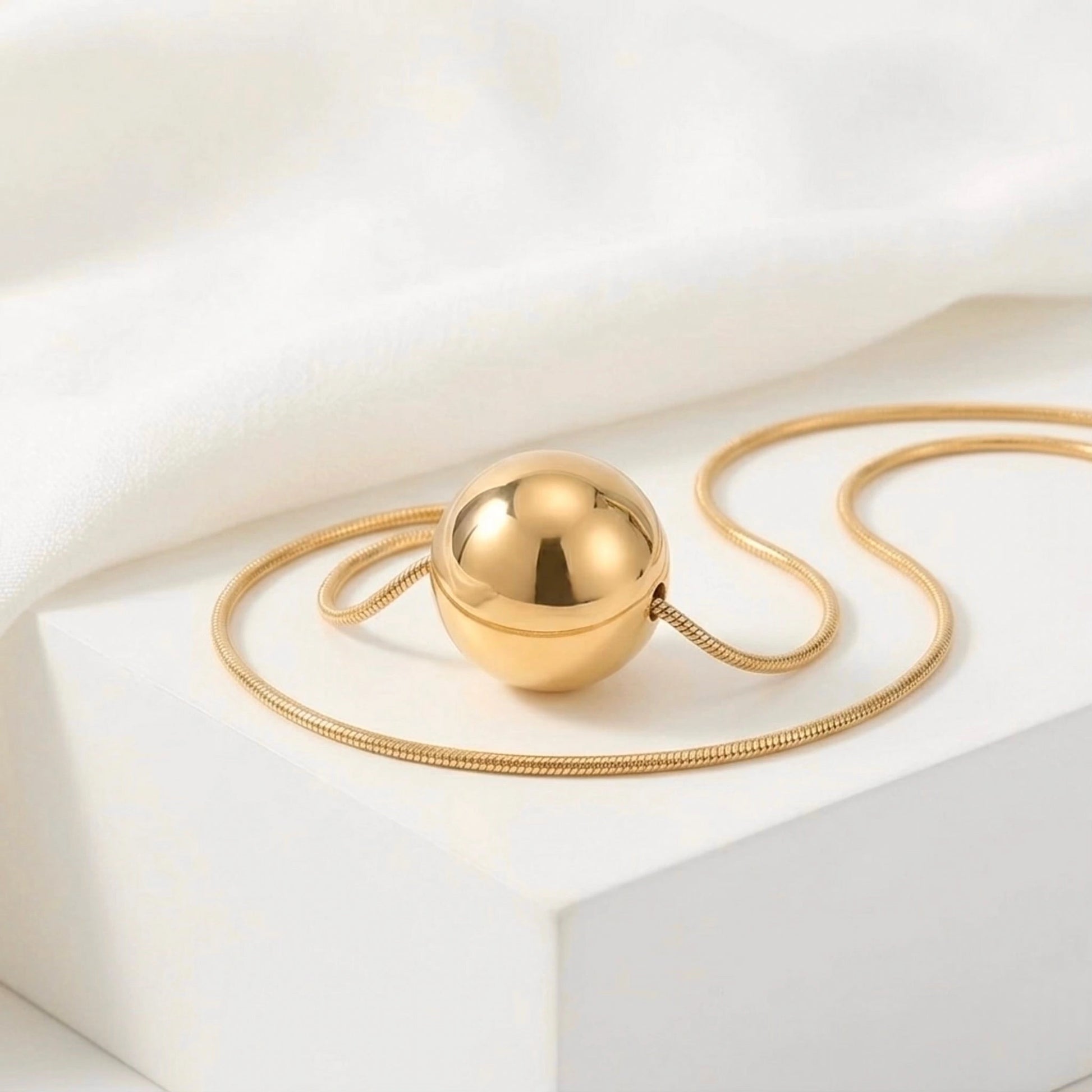 BEHI MILANO Chic Necklace — gold sphere pendant on snake chain displayed on marble pedestal