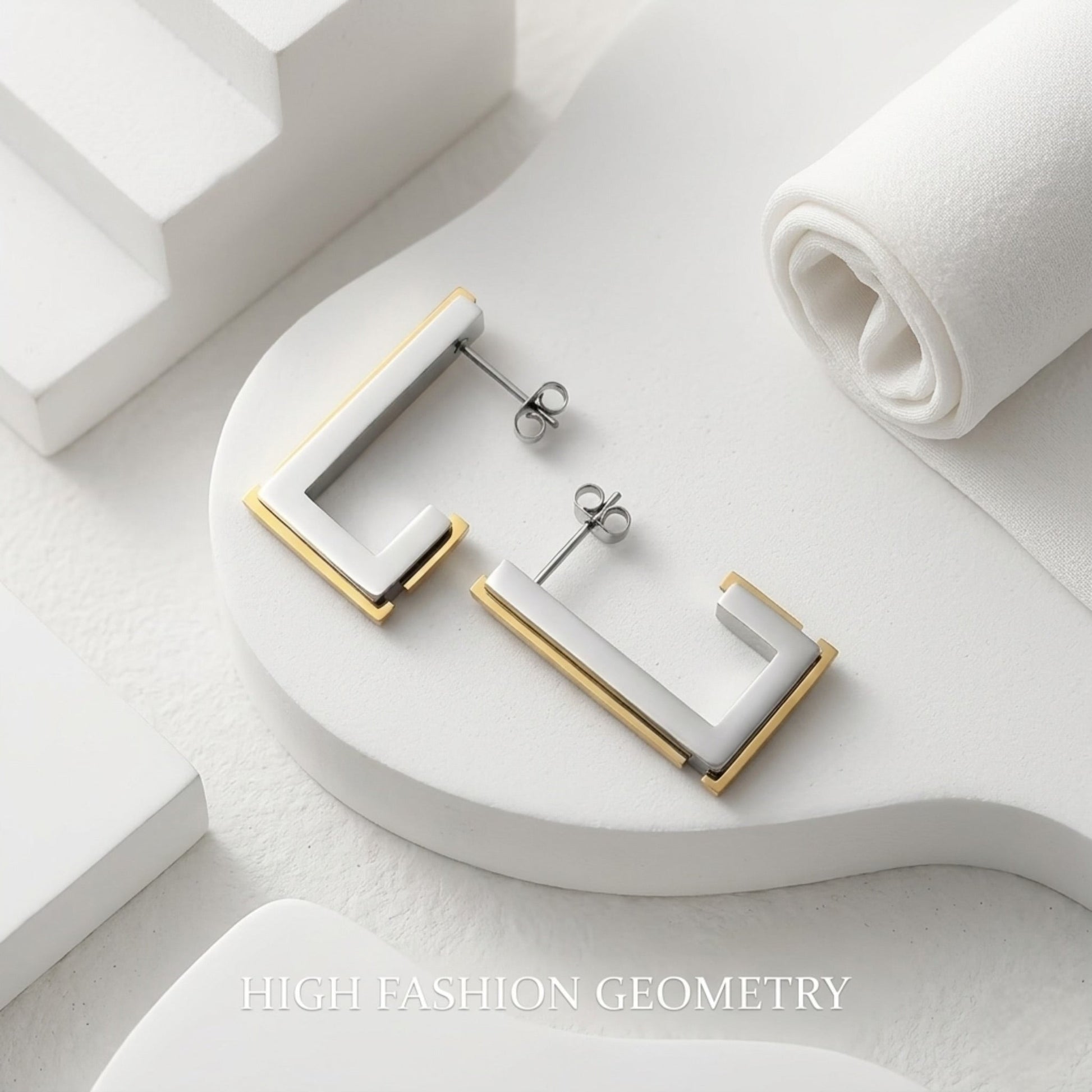 BEHI MILANO Cindy Earrings — two-tone gold and silver rectangular earrings on white architectural display