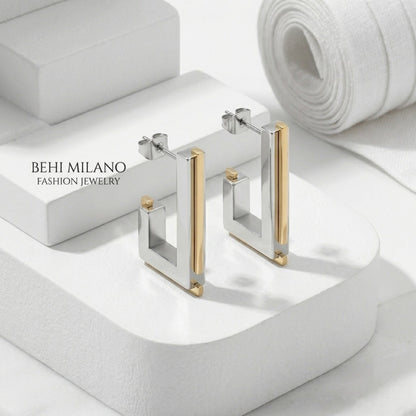 BEHI MILANO Cindy Earrings — pair of silver and gold geometric studs standing on white pedestal