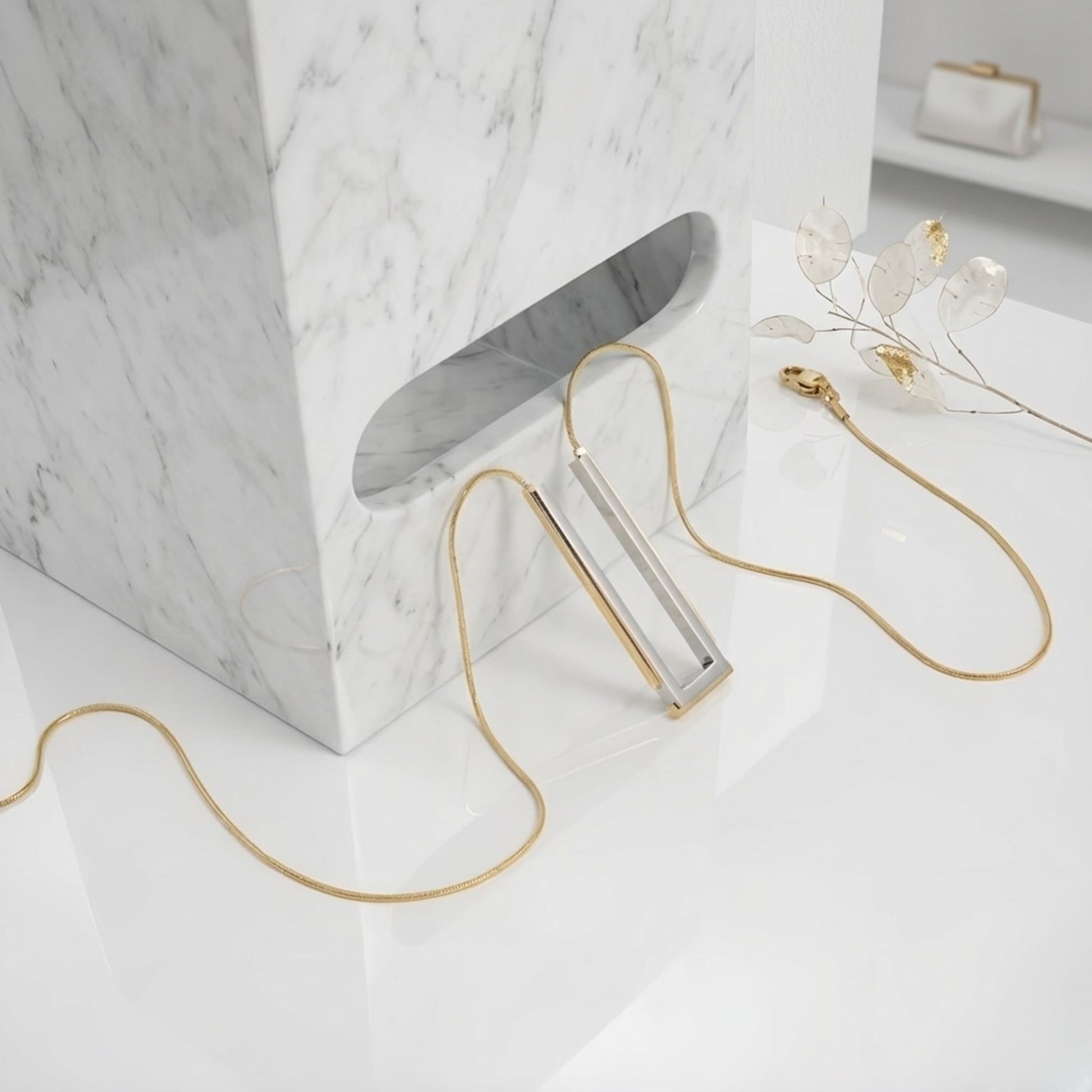 BEHI MILANO Cindy Necklace — silver and gold rectangular necklace draped over white marble block