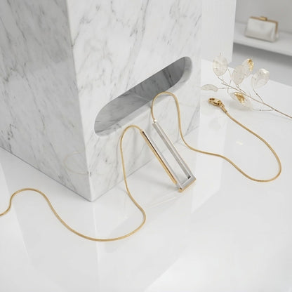 BEHI MILANO Cindy Necklace — silver and gold rectangular necklace draped over white marble block