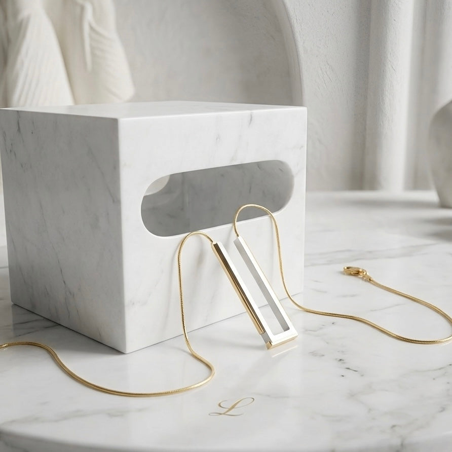 BEHI MILANO Cindy Necklace — two-tone geometric pendant displayed on white marble pedestal