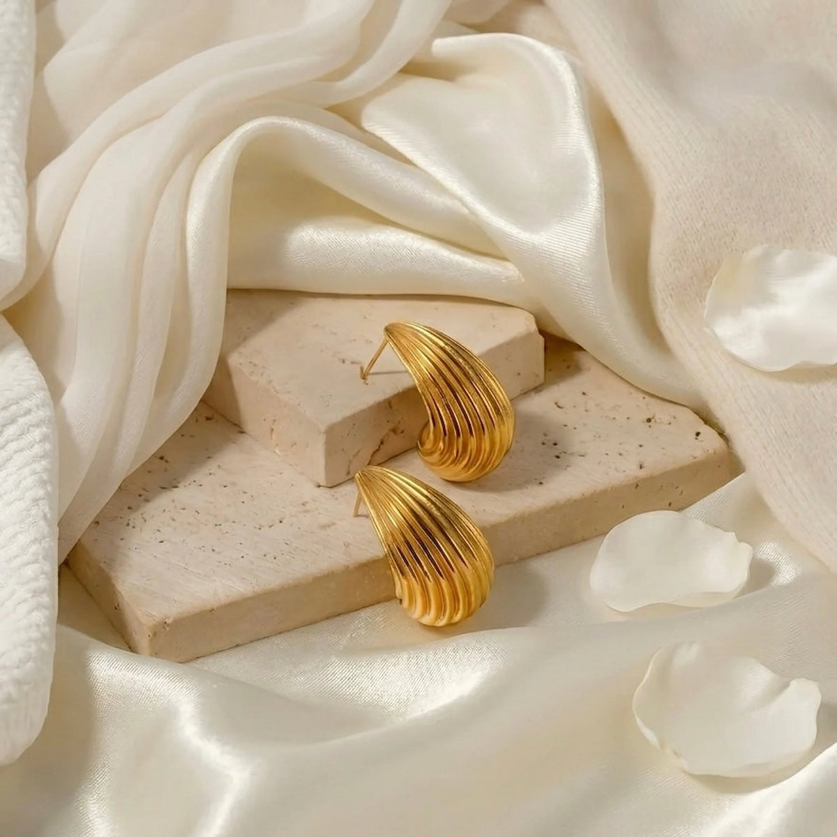 BEHI MILANO Claire Earrings — gold ribbed studs on beige stone block with white flower petals