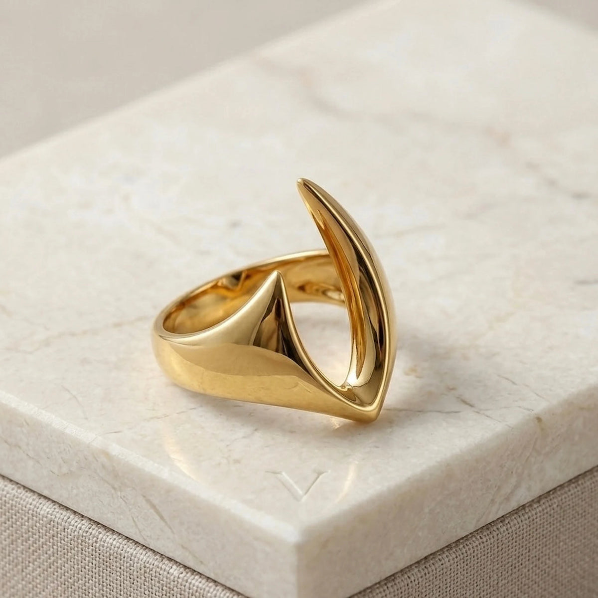 BEHI MILANO Clarissa Ring — gold blade shape statement ring resting on white marble pedestal