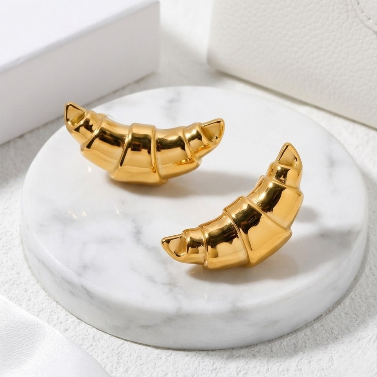 BEHI MILANO Cornetto Earrings — gold croissant drop stud earrings on round marble pedestal