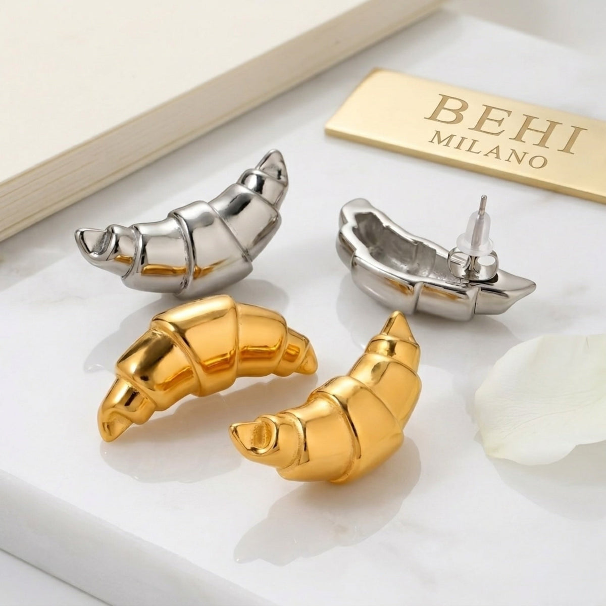 BEHI MILANO Cornetto Earrings — gold and silver croissant studs on white marble tile with brand logo card