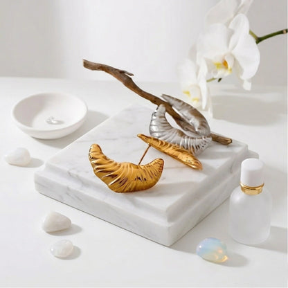BEHI MILANO Croissant Earrings — 18k gold ribbed earrings resting on white marble tray with orchid blossoms