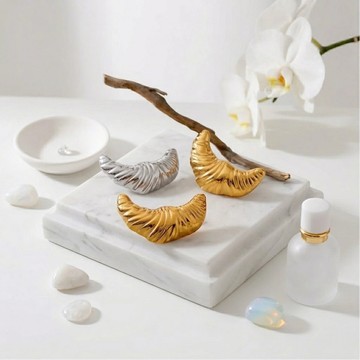 BEHI MILANO Croissant Earrings — gold and silver ribbed drop earrings displayed with wooden branch on marble tile