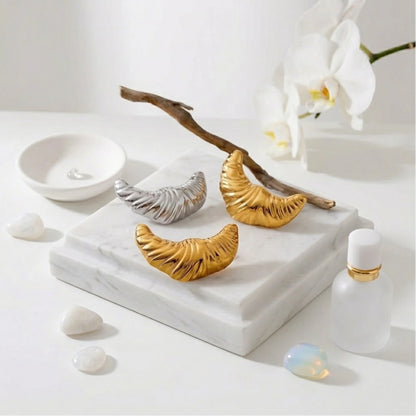 BEHI MILANO Croissant Earrings — gold and silver ribbed drop earrings displayed with wooden branch on marble tile