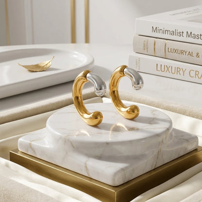 BEHI MILANO Dafne Earrings — close-up view of gold and silver curved hoops on white marble pedestal