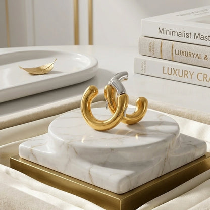 BEHI MILANO Dafne Earrings — two-tone gold and silver hoops displayed on round white marble pedestal next to art books