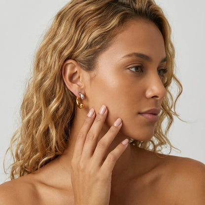 BEHI MILANO Dafne Earrings — model with curly blonde hair wearing two-tone gold and silver fluid hoop earrings