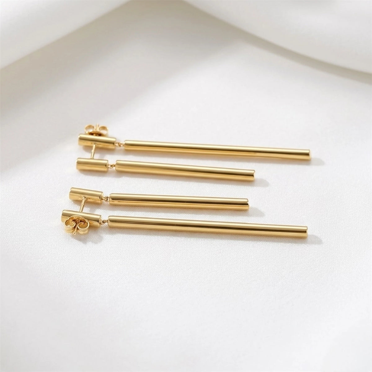 BEHI MILANO Deffi Earrings — gold 18k plated linear drop earrings laying on soft white background